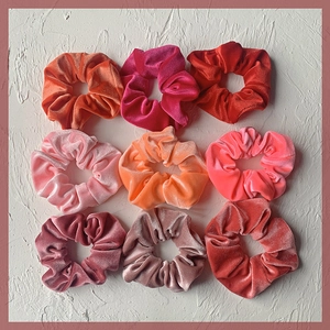Set of 9 velvet hair scrunchies in warm pink and orange tones on a stone texture