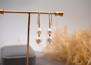 Detailed close-up of Baroque pearl earrings with gold hooks on a display stand