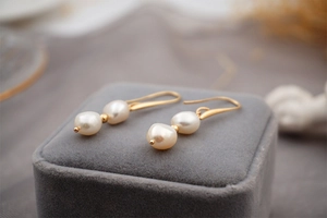 Detailed close-up of golden hook earrings featuring two white baroque pearls and a small gold bead