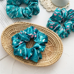 Detailed view of teal velvet scrunchies with pink geometric patterns in a lifestyle setting