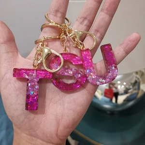Macro shot of resin alphabet keychains T S U with glitter sequins and gold lobster clasps