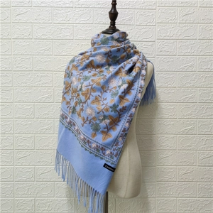 Detail of light blue cashmere scarf with colorful floral embroidery and long fringes