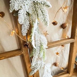 Snowy Christmas garland with LED lights, pine cones and wooden stars on rustic wood window