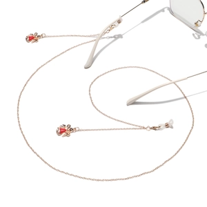 Detail of gold metal eyewear chain featuring red enamel bow pendants and anti-slip loops