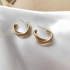 Detail view of matte gold twisted geometric earrings on soft white satin fabric