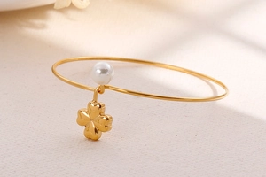 Detail of gold-plated bangle featuring a white pearl and solid clover charm