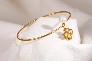 Close-up of gold stainless steel bangle with white pearl and four-leaf clover charm
