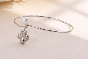 Detail of silver stainless steel bangle with white pearl and four-leaf clover pendant