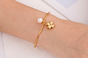 Detailed view of a gold clover charm and white pearl on a stainless steel open bangle