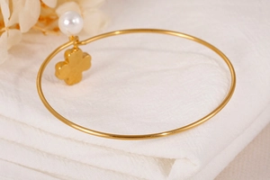 Detailed view of a gold bangle featuring a delicate pearl and a four-leaf clover pendant