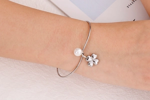 Close-up of women's silver stainless steel bracelet with white pearl and clover charm