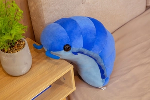 Close-up of a blue plush woodlouse toy on a bed with cozy bedroom decor background