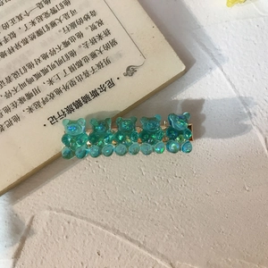 Green translucent gummy bear hair clip with gold metal base on a white surface