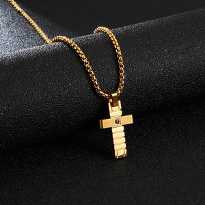 Macro shot of a golden box chain necklace with a black stone-encrusted cross pendant
