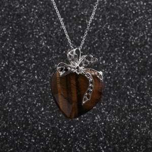 Collier pour femme avec nœud argenté et pendentif cœur en œil de tigre sur fond noir