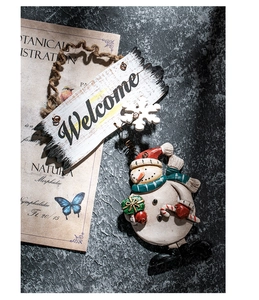 Close-up of Christmas snowman welcome wreath hanging on vintage botanical paper background