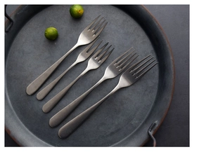 Detail of five matte dark gray stainless steel forks displayed on a round metal tray