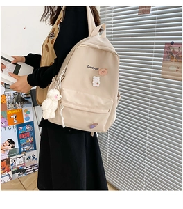 Detail of beige canvas backpack with cute plush bear pendant and cartoon badges