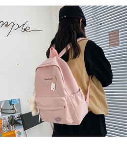 Pink canvas backpack with cute bear pendant and badges worn by model in a room