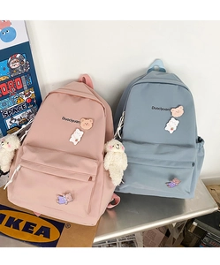 Pink and blue nylon backpacks featuring cute bear badges and plush charms in a lifestyle set