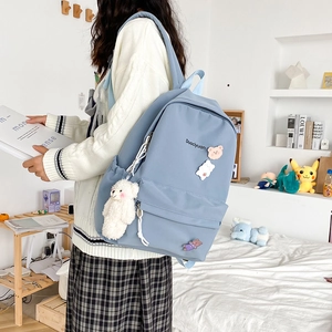 Close-up of blue canvas backpack featuring cute bear badges and a white plush pendant