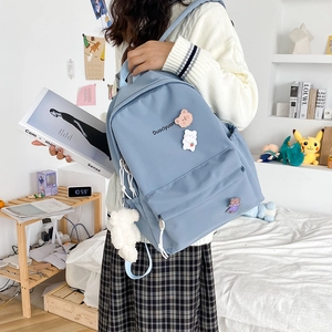 Detail of light blue school backpack featuring cute bear badges and a white plush pendant