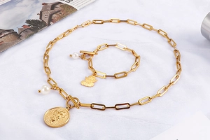 Detailed view of golden paperclip chain necklace and bracelet with pearl and angel coin