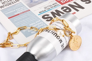 Close-up of golden link bracelet with pearl charm and angel coin toggle clasp