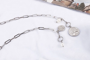 Détail des pendentifs arbre de vie et perles sur un collier en chaîne d'acier chic
