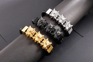Dettaglio di tre braccialetti a testa di lupo in oro, nero e argento su pelle intrecciata
