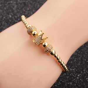 Golden beaded crown bracelet set with micro-paved crystals on a black display stand