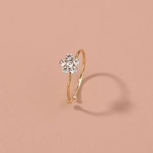 Adjustable gold flower ring featuring six white rhinestones on a warm pink background
