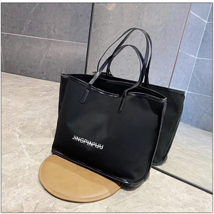 Close-up of a black tote bag with white lettering and patent leather trim on a marble floor
