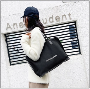 Outdoor shot of a black canvas tote bag with JINGPINPIJU print and glossy shoulder straps