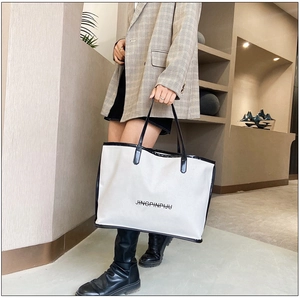 Detail of a large white tote bag with black handles and JINGPINPIJU printed text