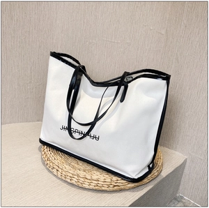 Close-up of white tote bag with black trim and JINGPINPIJU text on textured surface