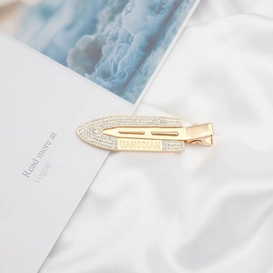 Macro detail of gold-plated hair clip with inlaid rhinestones and engraved UANODIAM text