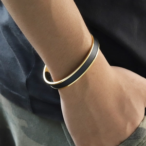 Close-up of minimalist black leather and gold titanium steel open cuff bracelet on wrist