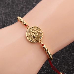 Goldenes Perlenarmband mit roter Kordel, Tierkreis-Anhänger und bunten Steinen auf Schwarz