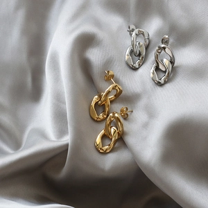 Macro detail of link chain earrings in gold and silver finish on silk fabric