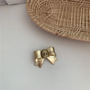 Baroque style gold bow brooch with embossed portrait pearl detail on white background