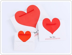 Three sizes of white paper gift bags with red heart pattern and rope handles