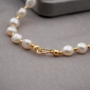 Baroque freshwater pearl necklace with golden S-hook clasp on grey fabric background