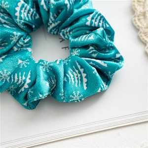 Close-up of teal velvet scrunchie with white Christmas tree patterns and soft texture