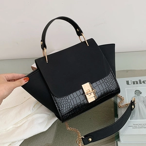 Chic black trapeze handbag with matte leather panels and gold chain strap in minimalist setting