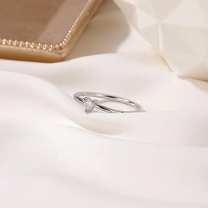 Close-up of minimalist silver heart ring with sparkling zircon on soft white silk fabric