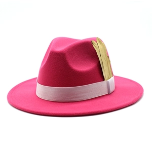 Detail of rose pink fedora hat featuring white ribbon band and golden feather ornament