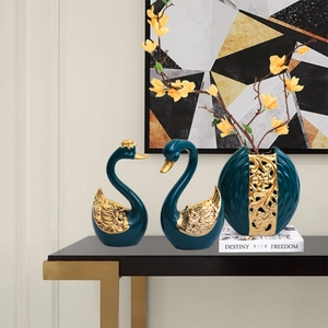 Nordic emerald and gold swan figurines with matching floral vase on a modern console table