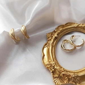 Detail of matte and polished gold twisted hoop earrings on white silk fabric background