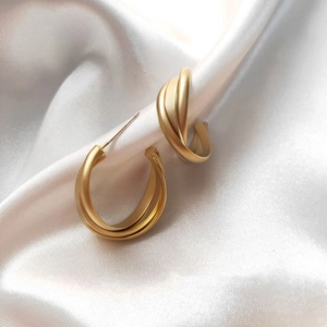 Detailed shot of matte gold twisted hoop earrings on white silk fabric background